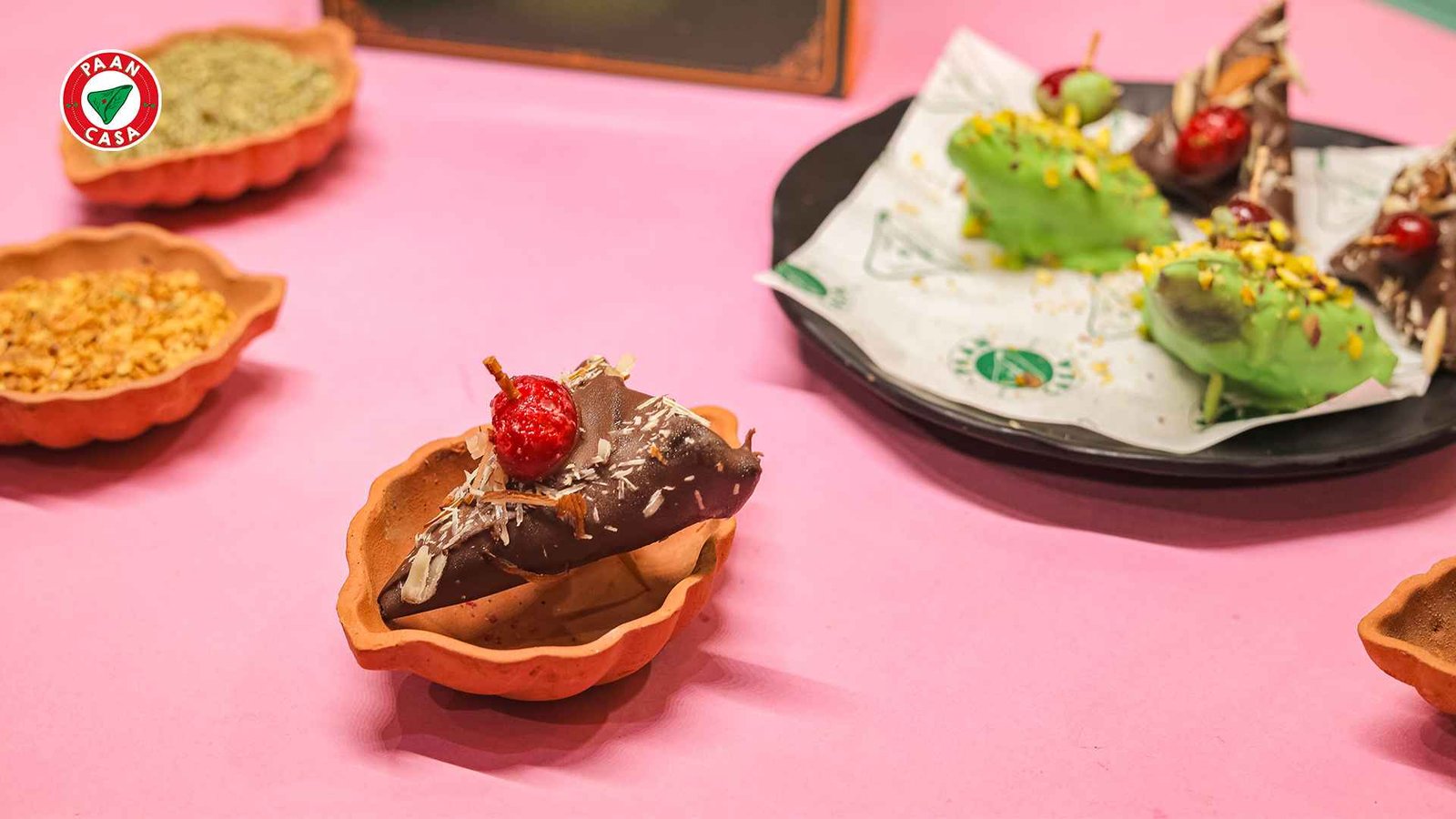 Chocolate-coated paan served in a decorative bowl with coconut shavings and a cherry garnish, alongside colorful fusion paan creations.