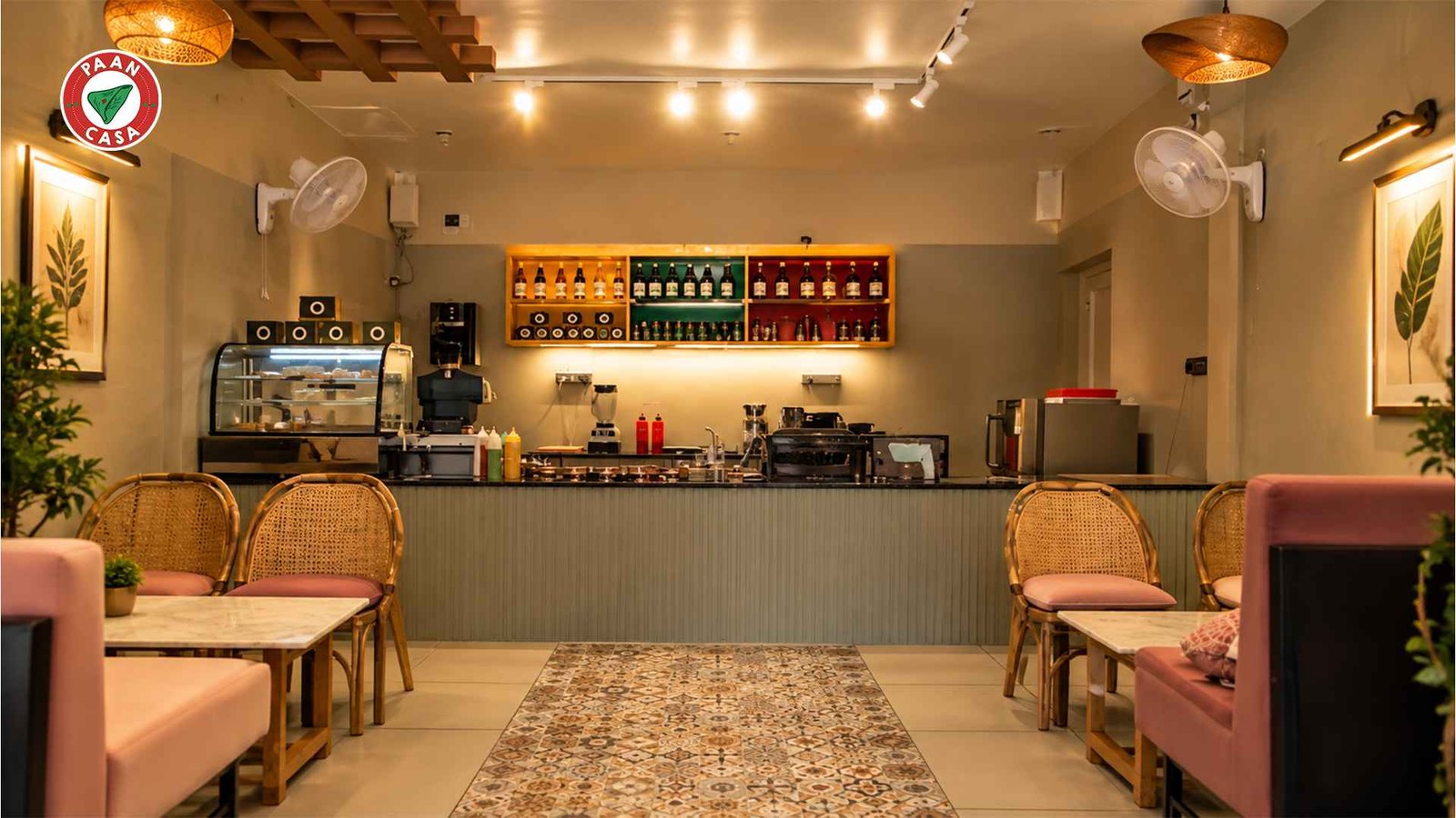 Warmly lit Paan Casa cafe interior with seating, counter, display case, and beverage shelves.